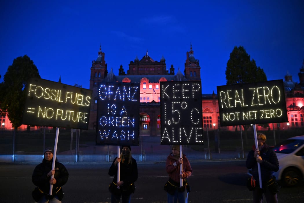 Climate activists hold illuminated signs and a banner protesting against the use of fossil fuels on the sidelines of the COP26 Climate Conference, at Kelvingrove in Glasgow, Scotland on November 3, 2021.