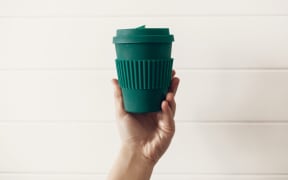 Zero waste concept. Hand holding stylish reusable eco coffee cup on white wooden background. Green Cup from natural  bamboo fiber. Ban single use plastic. Make a choice.