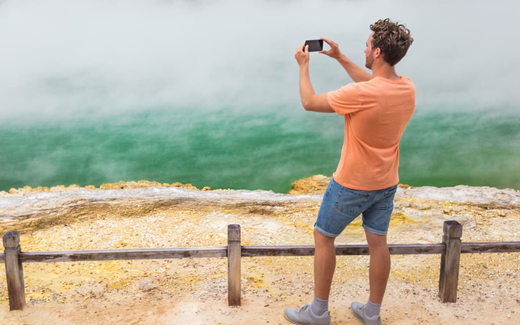 New Zealand travel tourist taking phone picture of famous attraction Champagne pool, Waiotapu.  Rotorua,