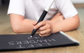 Left-handed child with a marker writes words on a notebook.
