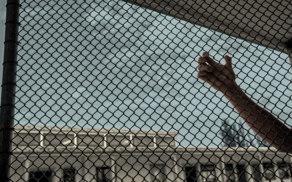 A hand holds onto the wire in prison