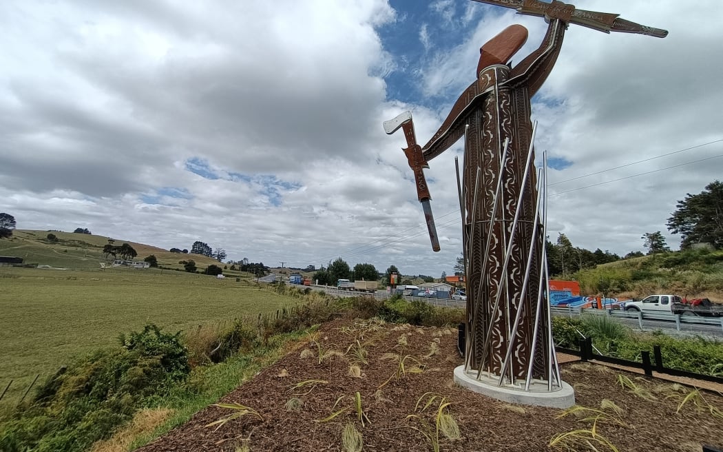 The warrior pou stands at the corner of State Highway 1 and the road to Ruapekapeka, between Hukerenui and Towai. The interpretation panel and canon are on the site of the British camp at Ruapekapeka. The canon points directly at the pa on the skyline.