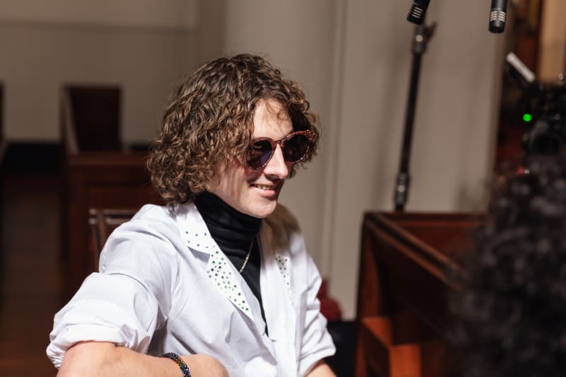 Ari Kerssens is smiling, seated at a piano in a church hall.