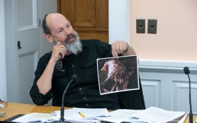 Steve Abel holds up an image of pigs in a farrowing crate during a scrutiny week hearing with Minister Andrew Hoggard.