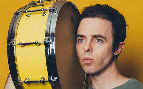 Publicity photo of American composer Daniel Temkin with a side drum on his shoulder.
