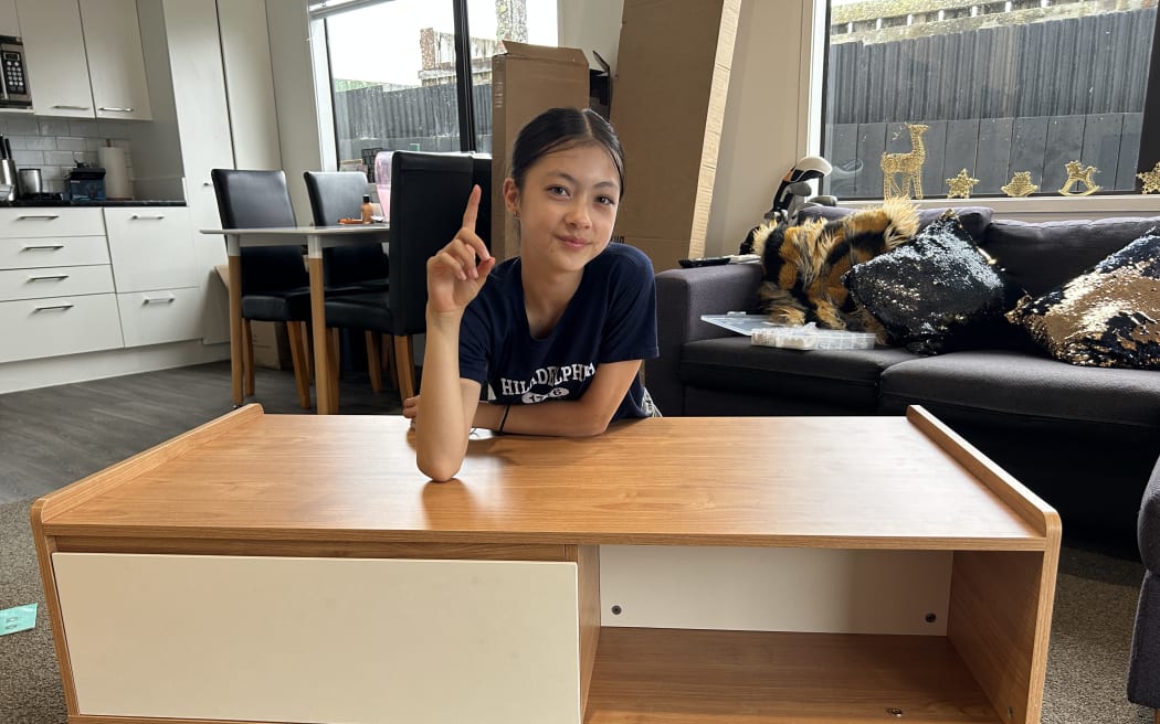 Picture of a young woman smiling at camera, sitting behind a coffee table she has just built.