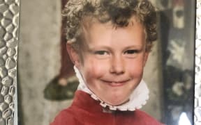 A framed picture of Emile as a young boy. He is wearing red velvet church robes and smiling at the camera.