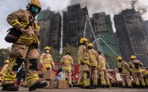 Firemen get ready after a major fire swept through several apartment blocks at the Wang Fuk Court residential estate in Hong Kong's Tai Po district on November 27, 2025. Hong Kong firefighters were scouring a still-burning apartment complex for hundreds of missing people on November 27, a day after the blaze tore through the high-rises, killing at least 44. (Photo by Dale DE LA REY / AFP)