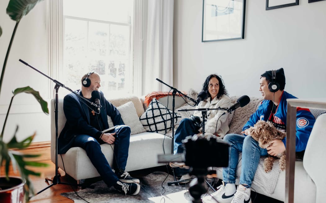 Reverend Frank Ritchie sits on a white corner couch with Moana Maniapoto and her son Hikurangi Jackson, who is holding his dog, Rocky.
