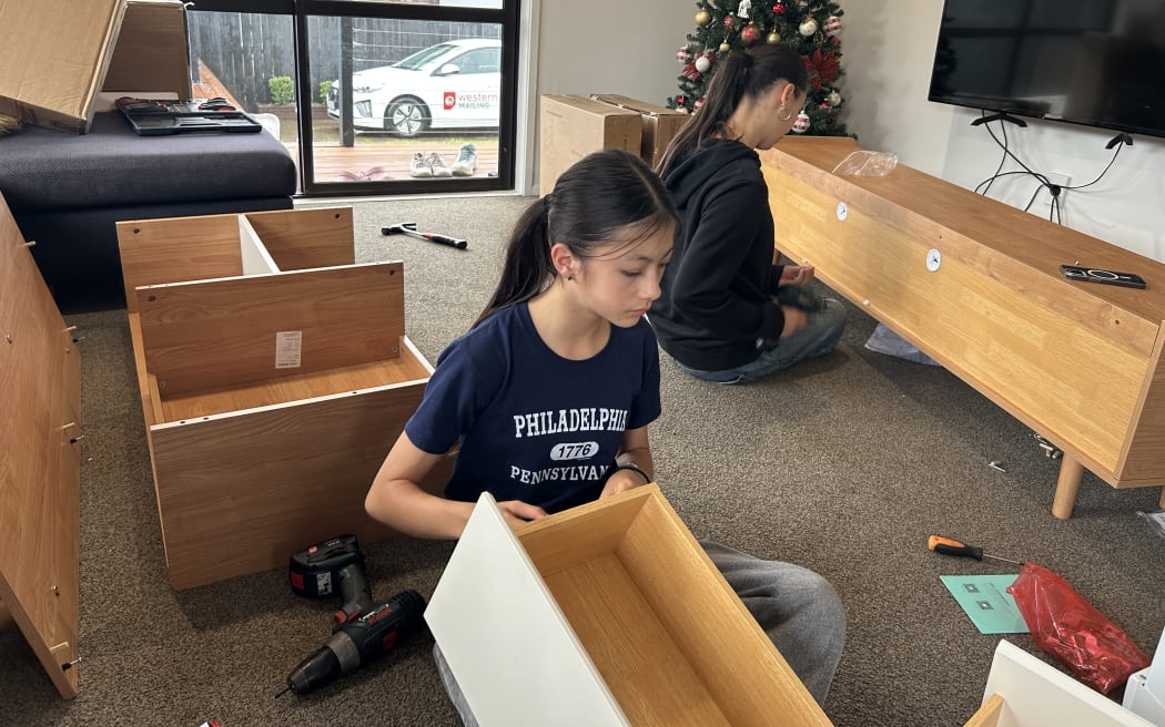Picture of two young women concentrating on putting furniture together.
