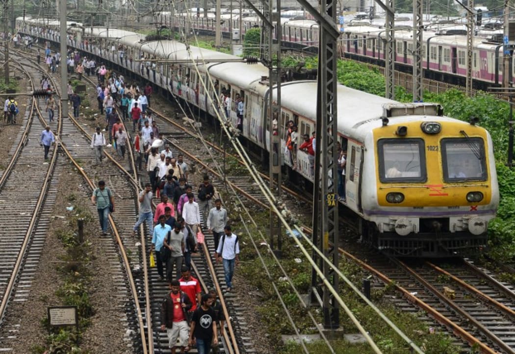 Indian commuters walk on railway tracks as train services slowly resume in Mumbai on 30 August, after heavy rains brought major flooding to the coastal city.