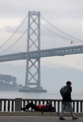 A homeless man lays on the sidewalk near the San Francisco/Oakland Bay Bridge