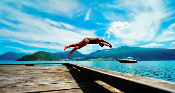A woman in a dark swimsuit diving into a lake.