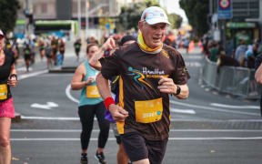 Rod Gill - a wearing brown shorts and t-shirt and white cap - runs ahead of a group of others along a road.