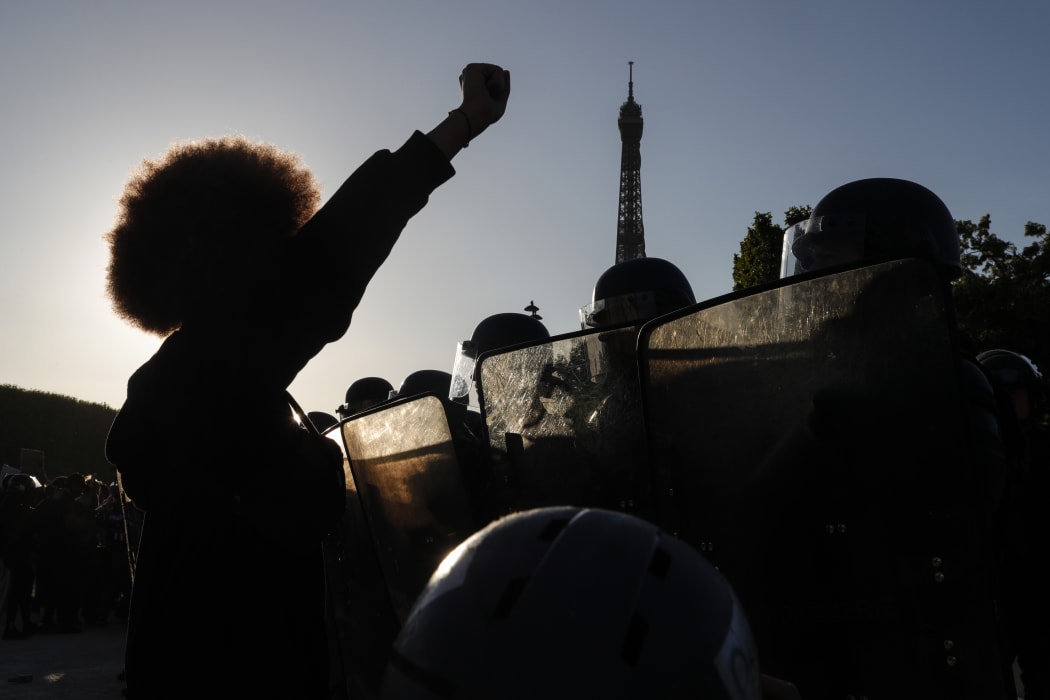 People raise their fists in front of riot policemen during a protest at the Champ de Mars, with the Eiffel Tower in background in Paris.