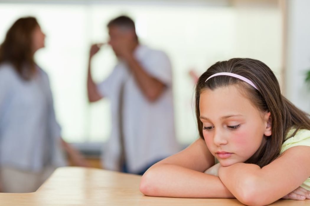 Photo of a sad girl with her parents arguing  behind her