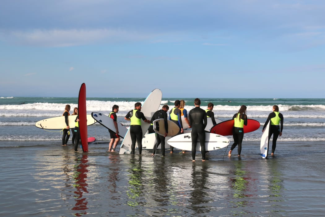 Farmers check out the waves with a surfing instructor before heading out for a lesson.