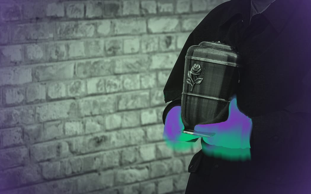 A funeral director carries a cremation urn, their hands are coloured to symbolise toxic chemicals