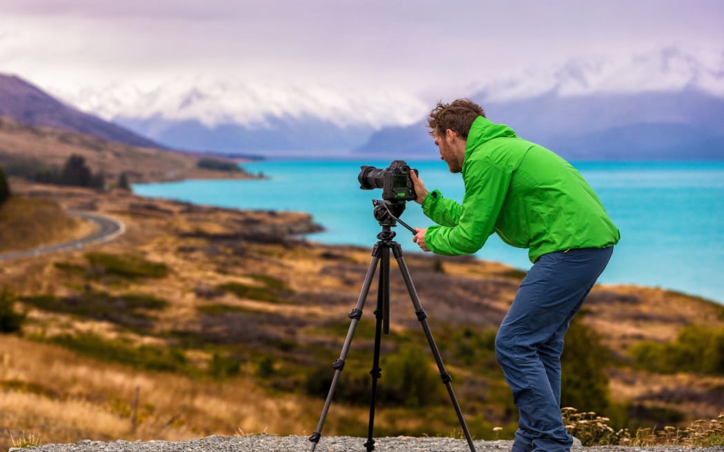 Travel photographer taking nature landscape pictures in New Zealand at sunset. Man shooting at Peter's lookout, famous tourist attraction at Pukaki Lake.