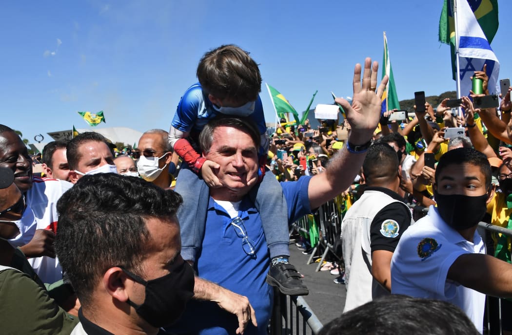 Brazilian President Jair Bolsonaro carries the son of a supporter on his shoulders as he greets supporters during a demonstration in Brasilia, during the Covid-19 coronavirus pandemic on May 31, 2020.