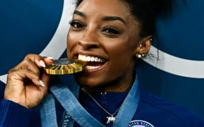 US' Simone Biles poses with her gold medal and a goat necklace after the podium ceremony for the artistic gymnastics women's all around final of the Paris 2024 Olympic Games at the Bercy Arena in Paris, on August 1, 2024. (Photo by Loic VENANCE / AFP)