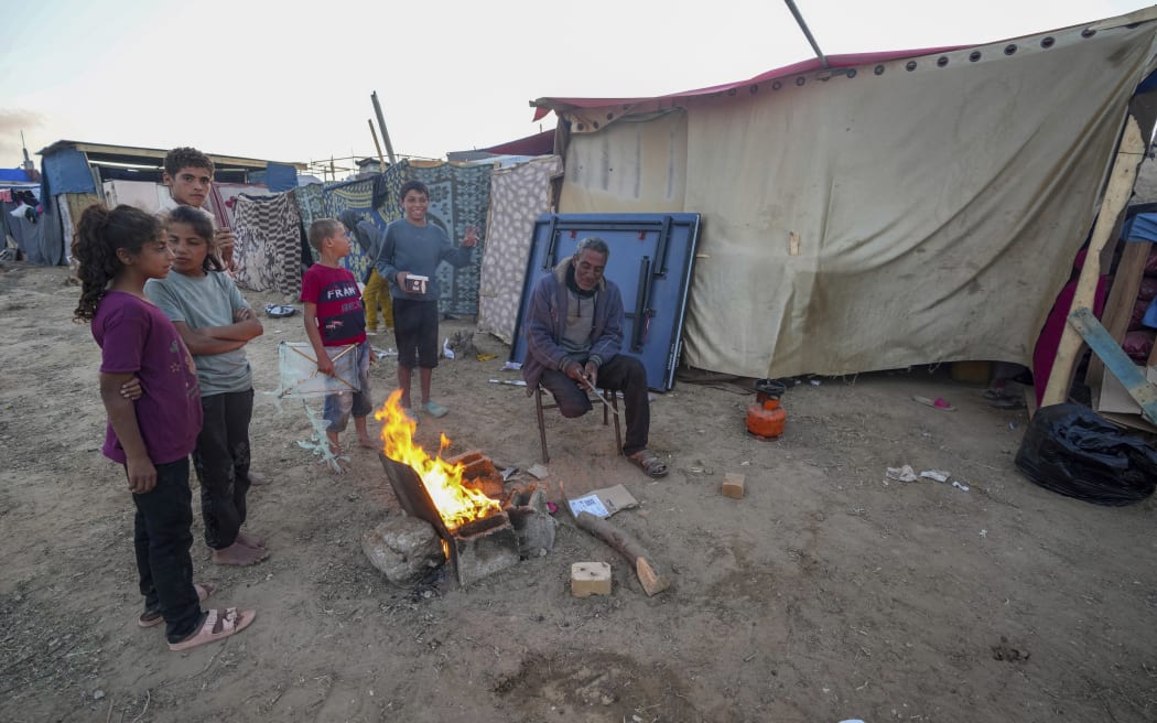 A Palestinian man and children sit next to a fire at a refugee camp in Deir al Balah, Gaza, on 13 May, 2024.