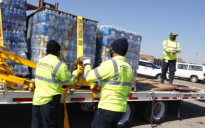 Workers with Houston Public Works unload pallets of water from a truck during a mass water distribution at Delmar Stadium on February 19, 2021 in Houston, Texas. and precipitation. Many Houston residents do not have drinkable water at their homes and are relying on city water giveaways.