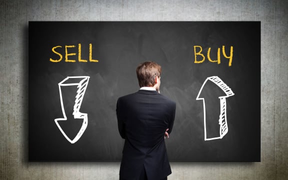 Businessman standing in front of a blackboard trying to decide whether to buy or to sell