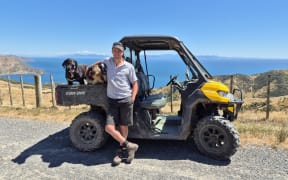 Hamish Best and his team of dogs on the back of a sidy-by-side overlooking the hilly farm with views out to the Cook Strait.