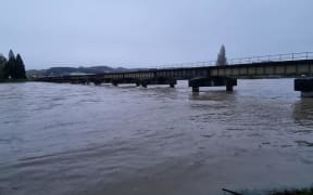 The Mataura River at Gore is flowing swiftly and some debris is caught under a rail bridge.