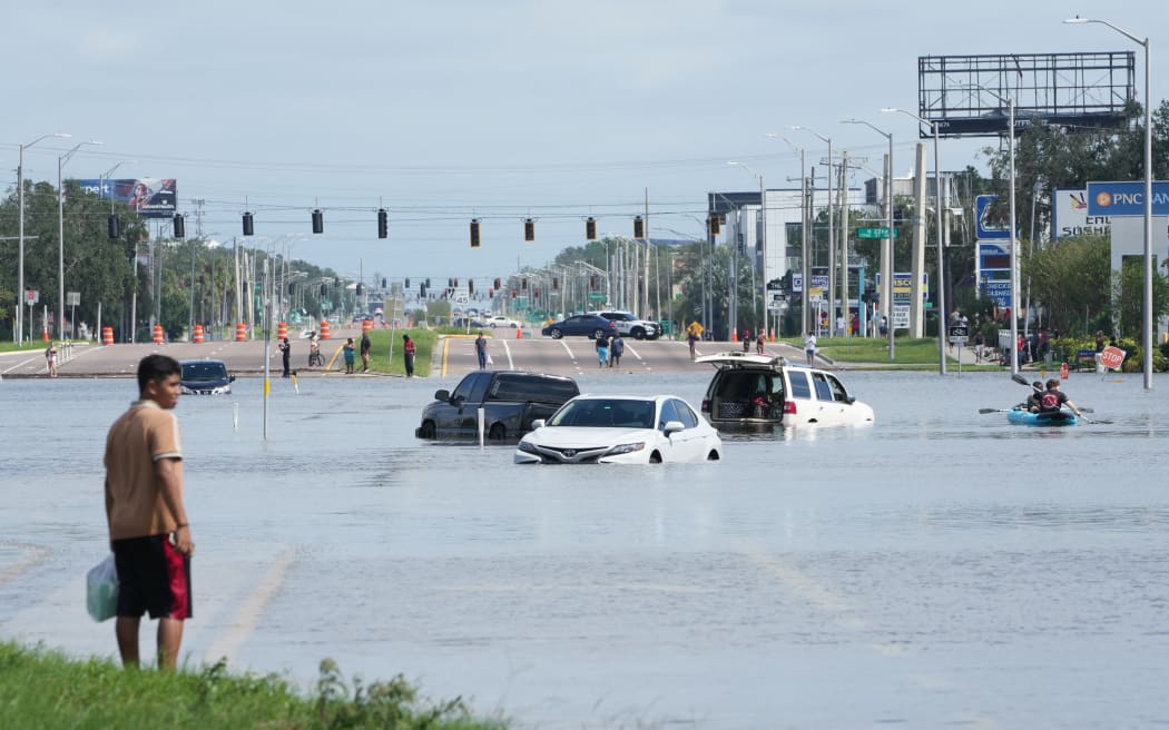 A young man looks on as cars are flooded in the water as the streets of the Southeast Seminole Heights section of Tampa due to Hurricane Milton on October 10, 2024 in Florida. Hurricane Milton tore a coast-to-coast path of destruction across the US state of Florida, whipping up a spate of deadly tornadoes that left at least four people dead, but avoiding the catastrophic devastation officials had feared. (Photo by Bryan R. SMITH / AFP)