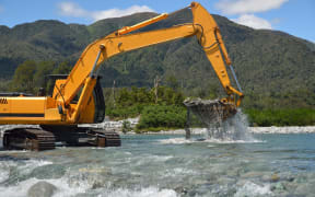 digger shifting shingle to deepen the channel in a flowing river, Westland, New Zealand