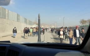 A busy street in Kabul. The photo is taken from within a car. People walk in both directions down the street.