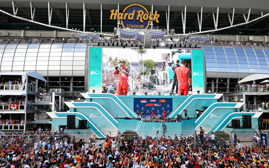 Fans cheer on the track as Oracle Red Bull driver Max Verstappen, Scuderia Ferrari driver Charles Leclerc and Scuderia Ferrari driver Carlos Sainz celebrate on the podium after the 2022 Miami Formula One Grand Prix.