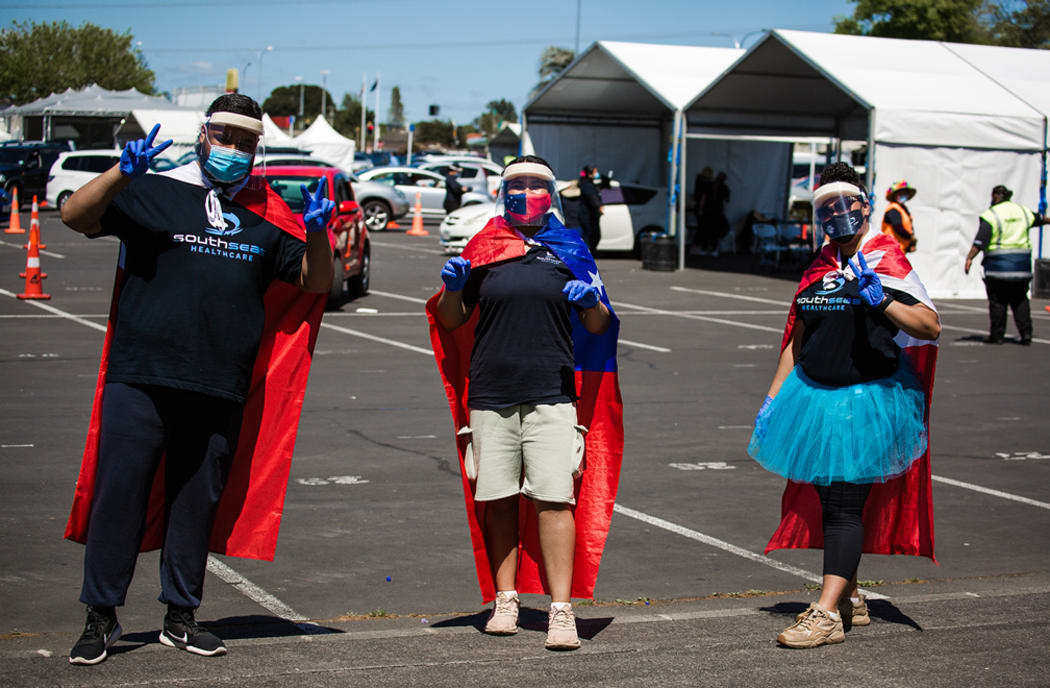 South Seas helpers drape flags across them as they support the Ōtara community at the Super Saturday vaccination event