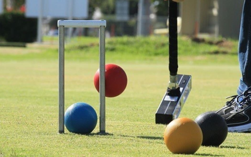 A close up of a mallet hitting colourful balls in a game of golf croquet.