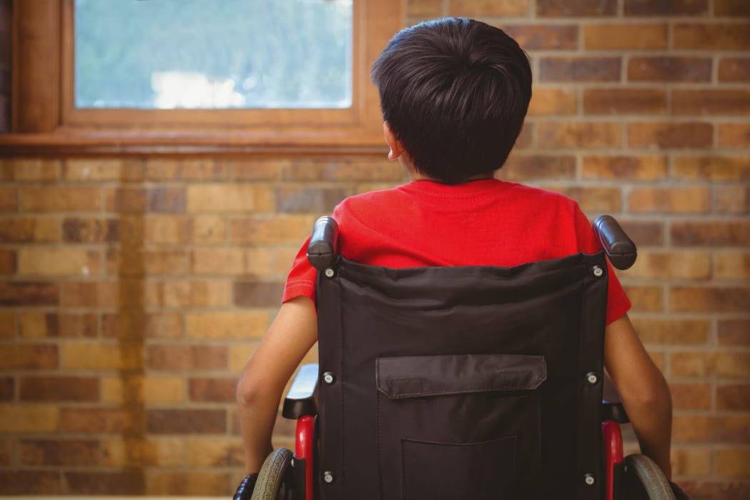 Rear view of little boy sitting in wheelchair in school