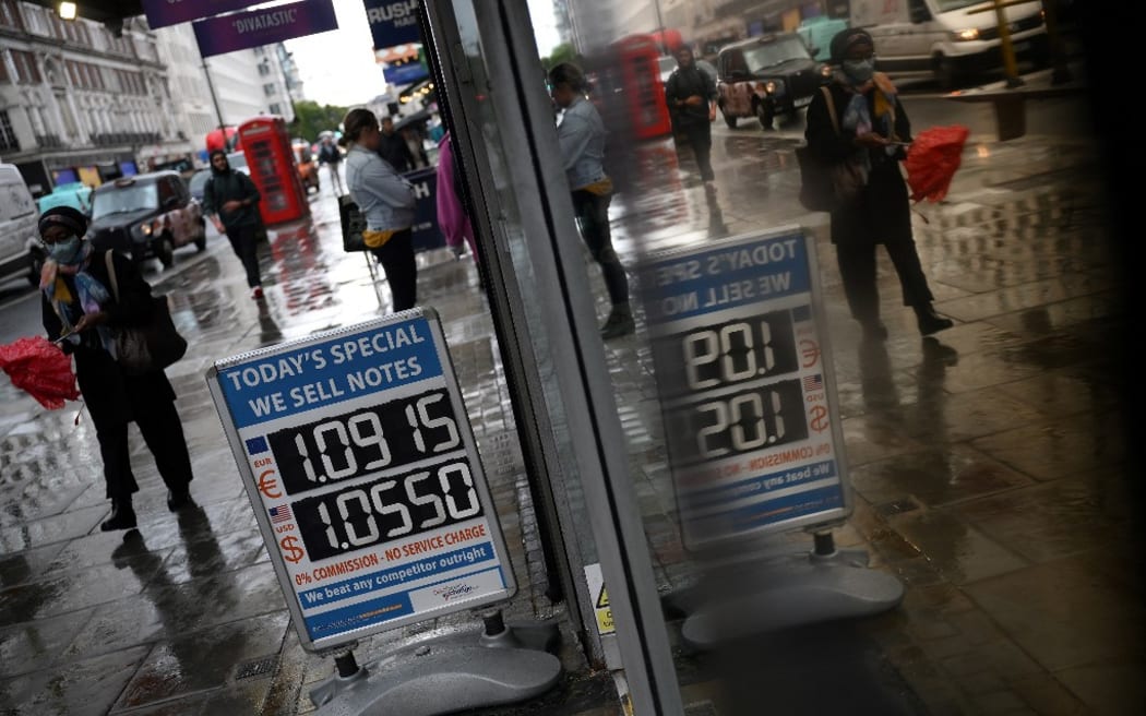 Pedestrians walk past a board displaying the price of Euro and US dollars against the British pound.