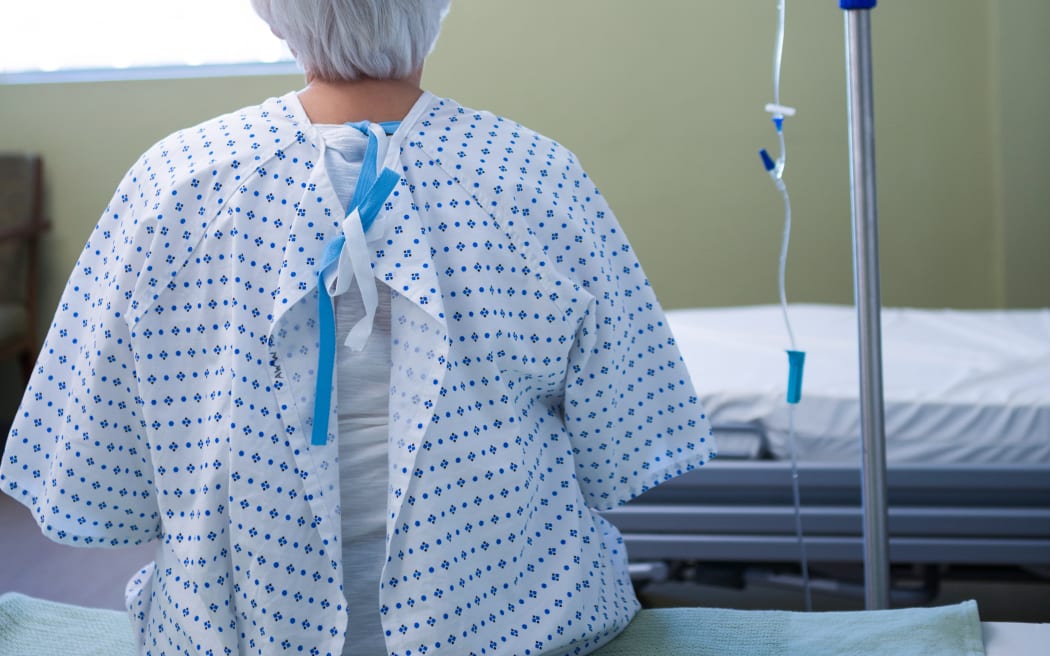 Rear-view of senior patient sitting on bed in hospital