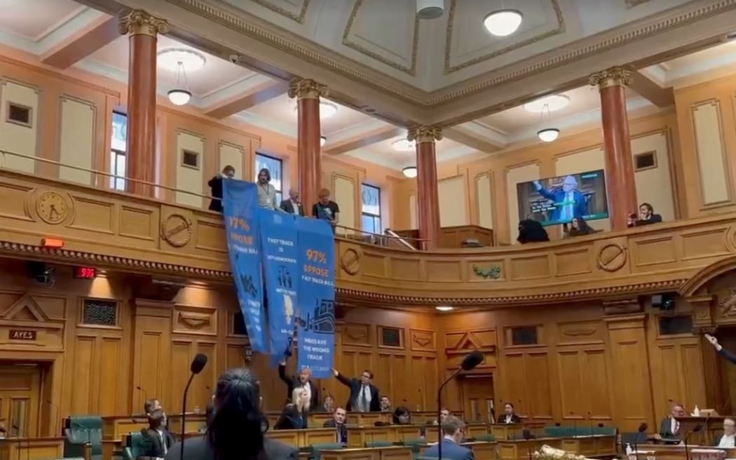 The third reading of the Fast-track bill was interrupted by 350 Aotearoa supporters who dropped banners from the public gallery while chanting.