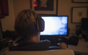Teenage boy with headphones playing video game in dark bedroom. (Photo by CAIA IMAGE/SCIENCE PHOTO LIBRARY / NEW / Science Photo Library via AFP)