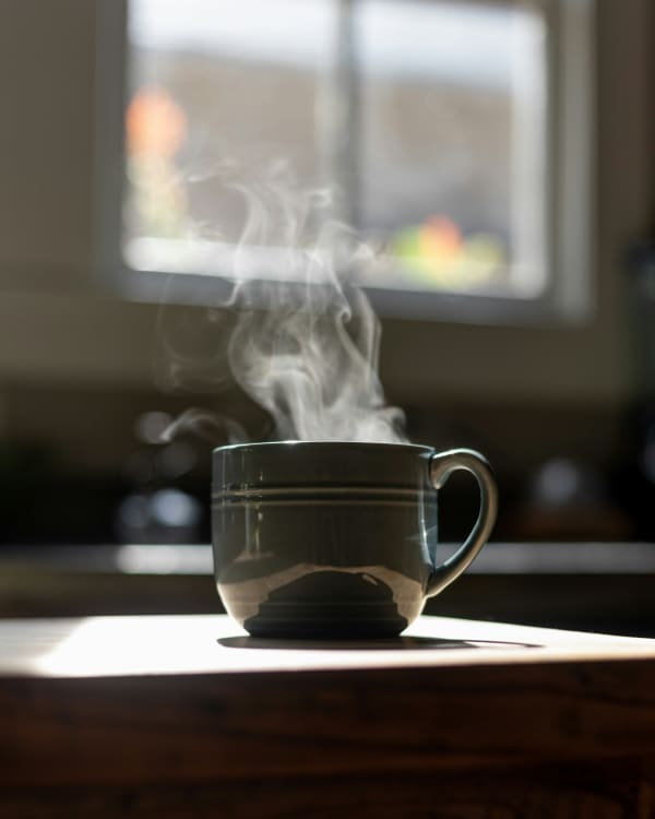 A steaming hot cup of water sitting on a bench.