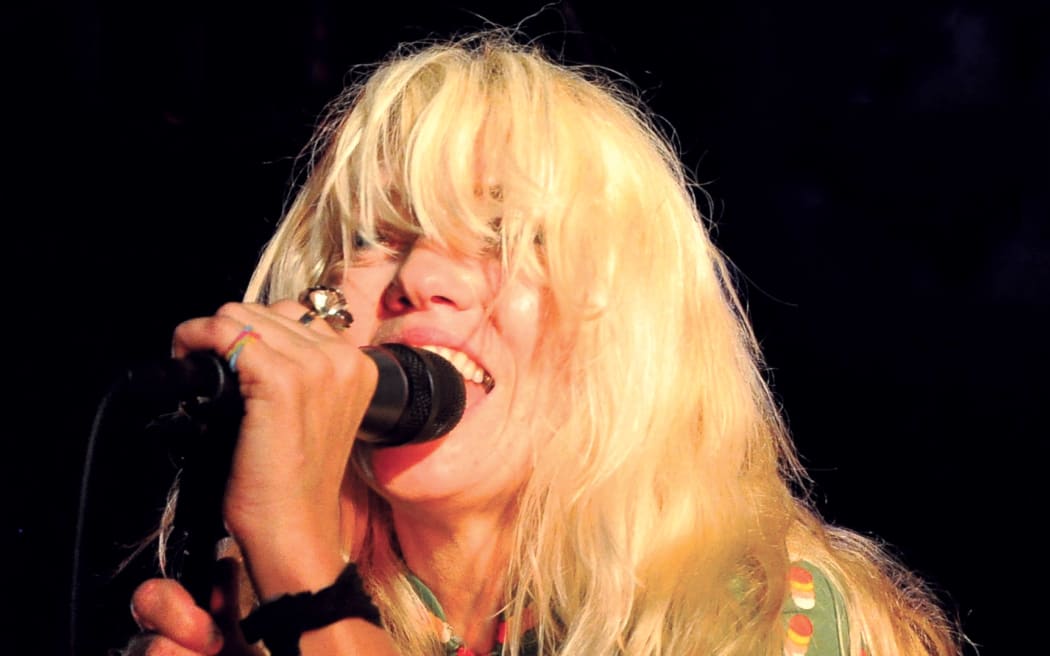 A woman with long blonde hair concealing her eyes sings into a microphone.
