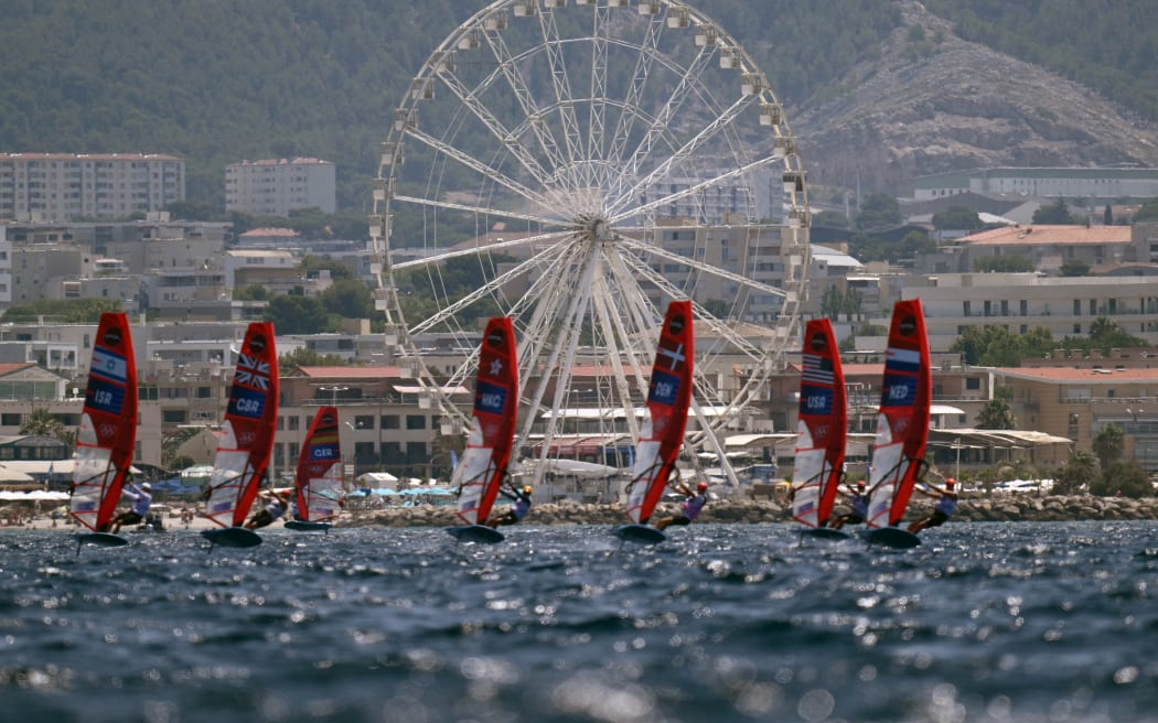 Windsurfers compete in front of a ferris wheel in Race 3 of the men’s IQFoil windsurfing event during the Paris 2024 Olympic Games sailing competition at the Roucas-Blanc Marina in Marseille on July 30, 2024. (Photo by Christophe SIMON / AFP)