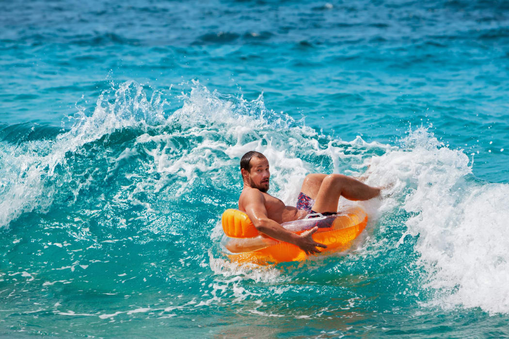Excited bearded hipster in inflatable ring have fun in beach surf. Funny man riding on tubing in breaking sea waves. Family travel lifestyle, swimming activities. Summer vacation on tropical island.