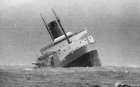 Wahine sinking in Wellington Harbour, 10 April 1968. Shows the boat leaning to one side, and another boat on the right. Taken by an unidentified Evening Post staff photographer.