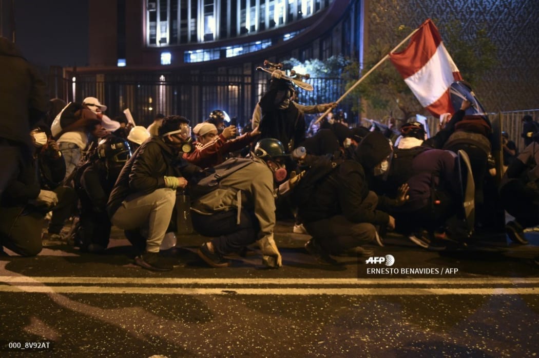Demonstrators, supporters of Peruvian ousted President Martin Vizcarra, holding a Peruvian flag, clash with riot ppolice during a protest against the government of interim president Manuel Merino.