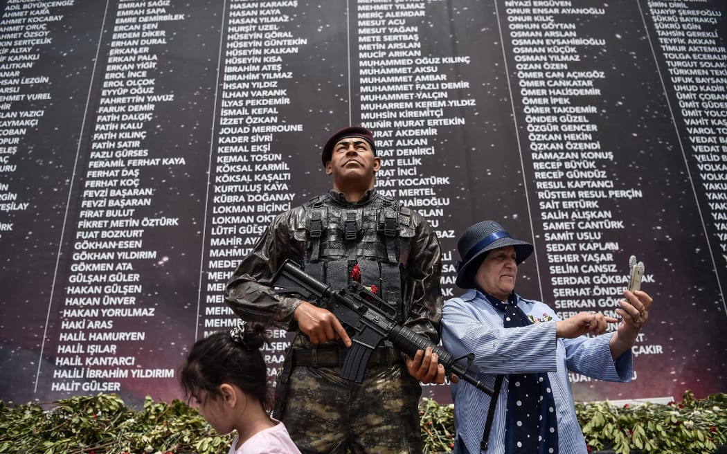 A woman takes a selfie picture with her mobile phone next to the statue of Omer Halisdemir, displayed on July 14, 2017 in Istanbul, in front of a memorial with the names of people killed last year during the failed coup attempt a year before.