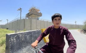 An Afghan boy cycles on a roadside behind the Bagram airfield while Afghan forces guard base towers in Kabul, Afghanistan.