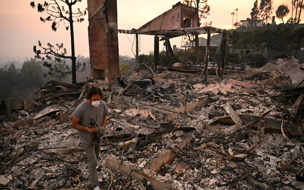 A man carries a bronze statue found amid the rubble of his parents' home, destroyed during the Palisades Fire, in Pacific Palisades, a neighborhood of Los Angeles, California, on January 9, 2025. The two largest fires burning in Los Angeles remain "zero percent" contained on January 9 despite firefighting operations, officials said, as they also vowed to tackle looting of evacuated homes. A 17,000-acre (6,900-hectare) blaze in Pacific Palisades has become "one of the most destructive natural disasters in the history of Los Angeles," said city fire chief Kristin Crowley, while a 10,000-acre fire in Altadena was also at "zero percent containment," said county fire chief Anthony Marrone. (Photo by Patrick T. Fallon / AFP)